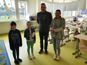 Dwoje przedstawicieli Rady Rodziców pozuje do wspólnego zdjęcia z dwiema uczennicami klasy drugiej. Jedna z dziewczynek trzyma w dłoniach kopertę.