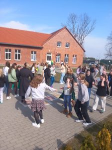 Uczniowie szkoły tańczą w parach na boisku. w tle widać ceglany budynek szkoły.