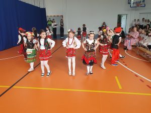 Uczniowie oddziału przedszkolnego wykonują taniec krakowiaka. Dzieci ustawione są w okręgu przodem do obiektywu.