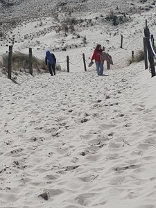 woje uczniów idzie wyznaczoną ścieżką po piaszczystym terenie. W tle widoczne są wydmy.