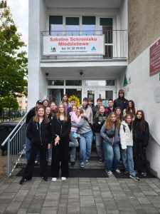 Uczniowie biorący udział w wycieczce pozują do wspólnego zdjęcia stojąc na schodach prowadzących do białego budynku. Na balkonie nad nimi zawieszony jest baner z napisem "Szkolne Schronisko Młodzieżowe tel. 91 32 70 613".