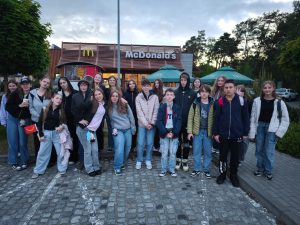 Uczniowie klasy siódmej biorący udział w wycieczce pozują do grupowego zdjęcia przed budynkiem McDonald's.