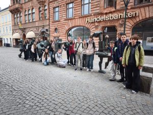 Uczniowie biorący udział w wycieczce pozują do wspólnego zdjęcia stojąc na brukowym pasażu. W tle widać zabudowania kamieniczne. Na jednym z budynków widnieje napis "Handelsbanken".