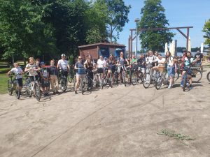 Uczniowie i ich opiekunowie biorący udział w rajdzie pozują do wspólnego zdjęcia stojąc przy swoich rowerach.