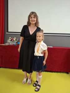 Wychowawczyni oddziału przedszkolnego pozuje do zdjęcia wraz ze swoją uczennicą. Dziewczynka ma zawieszony na szyi medal.