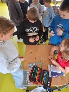 Grupa dzieci bawi się przy ławce grą Magnetic – prezentem z okazji Dnia Chłopaka. Na stole leży sznurek w kształcie koła, a w środku rozłożone są magnetyczne elementy.