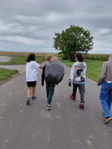 Trzech uczniów idzie asfaltową drogą. Chłopiec idący po środku ma zarzucony na plecy wypełniony śmieciami czarny worek.