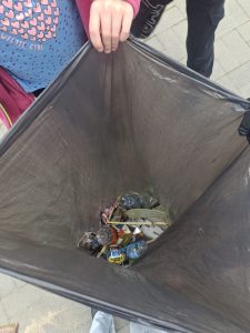 Uczniowie trzymają szary worek, w którym widoczne są drobne śmieci.