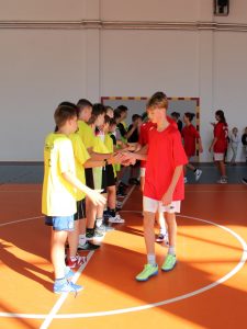Dwóch zawodników – jeden w czerwonej koszulce, drugi w żółtej – podaje sobie dłonie w geście sportowego zakończenia meczu.