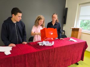 Troje uczniów liczy głosy po zakończeniu wyborów do samorządu. Na stole leżą karty wyborcze wysypane z czerwonej urny.