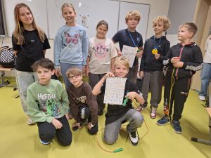 Dziewięcioro dzieci pozuje wspólnie w klasie. Dwoje dzieci w pierwszym rzędzie klęczy, reszta stoi. Kilkoro z nich trzyma dyplomy i medale, inne kolorowe skakanki. Na tablicy w tle widnieje napis „Dzień Chłopaka”.