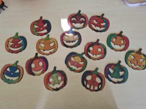 Kolorowe papierowe dynie z wyciętymi oczami i ustami, ułożone na stole. Każda dynia ma inny wzór i barwy, tworząc wesołą halloweenową dekorację.