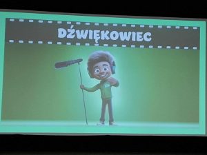 Na ekranie kinowym widoczna jest ilustracja postaci trzymającej mikrofon na statywie i noszącej słuchawki. Nad obrazem napis „Dźwiękowiec”.