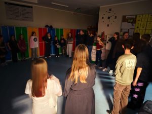 Uczniowie stoją w dużym kręgu na szkolnym korytarzu podczas zabawy andrzejkowej.