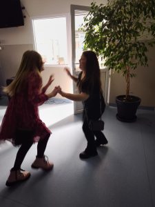 Dwie uczennice trzymają się za ręce i tańczą w jasnym holu szkoły.