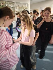 Uczennice uczestniczą w andrzejkowej wróżbie, stojąc w kolejce przed gablotą z pucharami.