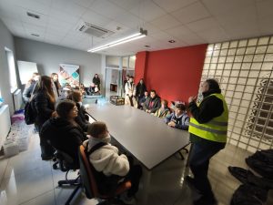 Uczniowie klasy VIII siedzą i stoją w sali konferencyjnej firmy HOLKAP, słuchając pracownika w kamizelce odblaskowej, który prowadzi prezentację na temat działalności przedsiębiorstwa.