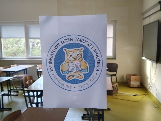 Plakat z logo Światowego Dnia Tabliczki Mnożenia przedstawiający sowę trzymającą karty z działaniami matematycznymi. W tle widać salę lekcyjną.