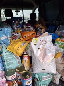 Wnętrze samochodu dostawczego wypełnione licznymi workami i puszkami karmy dla psów i kotów. Torby i opakowania w różnych kolorach ułożone są jedna na drugiej, zajmując niemal całe miejsce ładunkowe.