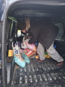 Uczeń pochylony we wnętrzu samochodu dostawczego układa worki z karmą dla zwierząt. W przestrzeni ładunkowej leży wiele toreb i opakowań z karmą.