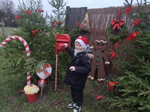 Dziecko wrzuca list do skrzynki na listy do Mikołaja przy ozdobionych choinkach.