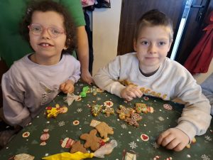 Dwoje dzieci z oddziału przedszkolnego siedzi przy stole i prezentuje udekorowane pierniki ozdobione lukrem oraz kolorowymi posypkami podczas warsztatów świątecznych.