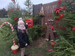 Dziecko wkłada list do czerwonej skrzynki „Letters to Santa” ustawionej wśród świątecznych dekoracji.