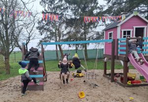 Dzieci bawią się na placu zabaw, korzystając z huśtawek, zjeżdżalni i konstrukcji do wspinania.