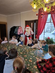 Dzieci siedzą przy stole i słuchają osoby przebranej za świętego Mikołaja podczas spotkania świątecznego.