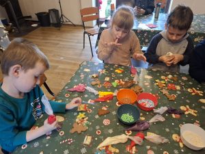 Dzieci dekorują pierniki przy stole, korzystając z kolorowego lukru i posypek.