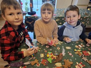 Troje dzieci prezentuje udekorowane pierniki, trzymając w dłoniach rękawy cukiernicze.