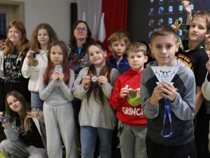 Uczniowie stoją w grupie obok prelegentki i prezentują medale maratońskie, które trzymają w rękach.