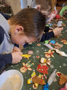 Dziecko koncentruje się na dekorowaniu piernika żółtym lukrem przy stole warsztatowym.