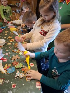 Dzieci z oddziału przedszkolnego dekorują pierniki lukrem i posypkami przy świątecznie nakrytym stole.