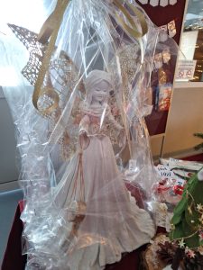 Zbliżenie na figurkę anioła w ozdobnym opakowaniu stojącą na stole z innymi świątecznymi wyrobami.