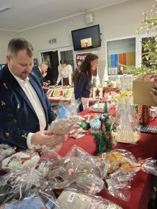 Osoba wybiera rękodzieło świąteczne spośród zapakowanych ozdób wystawionych na stole podczas kiermaszu.