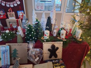 Stół kiermaszu bożonarodzeniowego z ręcznie wykonanymi choinkami, świecami i dekoracjami świątecznymi, każda z widoczną ceną.