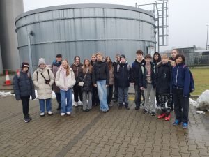 Grupa uczniów klasy VII stojąca na zewnątrz zakładu przemysłowego podczas wycieczki zawodoznawczej.