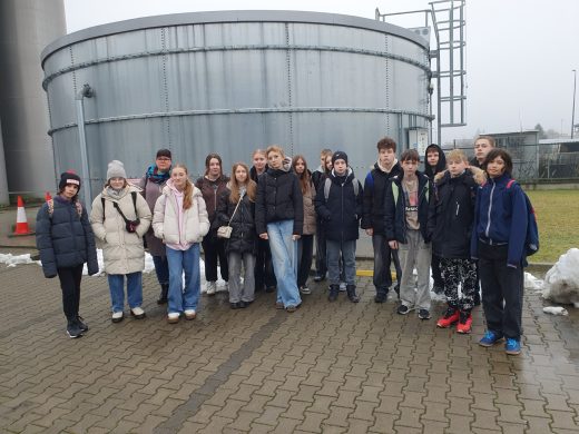 Grupa uczniów klasy VII stojąca na zewnątrz zakładu przemysłowego podczas wycieczki zawodoznawczej.