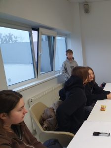 Uczniowie siedzący przy stole podczas spotkania informacyjnego w pomieszczeniu zakładu przemysłowego.