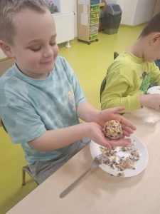 Uczeń prezentuje uformowaną kulę z ziaren i smalcu przeznaczoną dla ptaków.