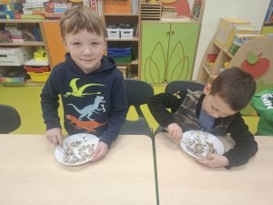 Dzieci z oddziału przedszkolnego siedzą przy stoliku i mieszają smalec z ziarnami w miseczkach.