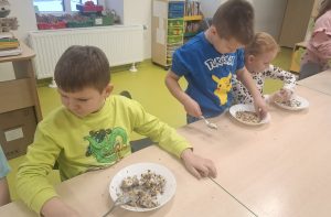 Grupa dzieci przy stoliku przygotowuje ekologiczne karmniki z ziaren i smalcu, ugniatając je w miseczkach.