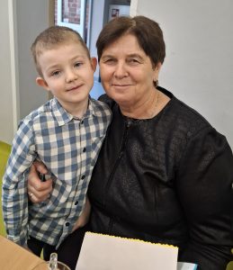 Chłopiec stoi obok starszej kobiety, która obejmuje go ramieniem; oboje pozują do zdjęcia podczas uroczystości w przedszkolu.