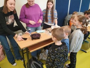 Uczniowie edukacji przedszkolnej obserwują eksperyment z głośnikiem wprawiającym w ruch cząsteczki soli.