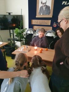 Uczniowie klasy 7 prezentują młodszym dzieciom eksperyment z sztucznym ogniem umieszczonym w mandarynce na stole podczas Dnia Nauk Przyrodniczych.