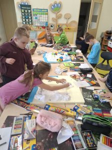 Dzieci pracują przy stolikach, wykonując makiety biegunów; na stołach znajdują się kredki, plastelina i papier.