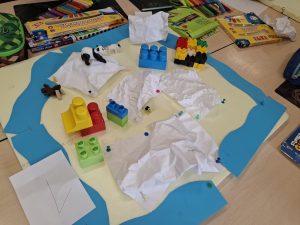 Makieta obszaru polarnego w trakcie tworzenia; widoczne klocki, papierowy lód oraz figurki zwierząt.