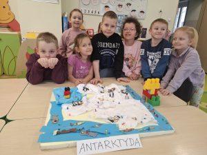 Dzieci pozują przy makiecie Antarktydy oznaczonej kartką z napisem „Antarktyda”.
