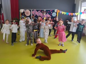 Uczniowie w przebraniach karnawałowych pozują do wspólnego zdjęcia na tle dekoracji z napisem „2026” na sali teatralnej.